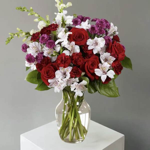 Bouquet of red roses, white alstroemeria, and purple carnations in a clear glass vase