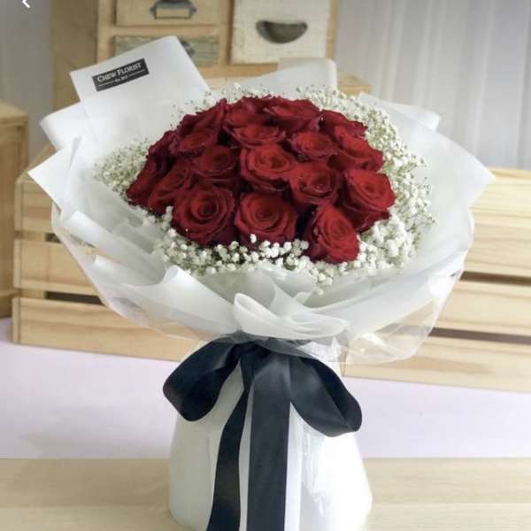 Bouquet of red roses wrapped in white paper with a black ribbon