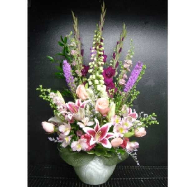 Tall pink and purple mixed flower arrangement with lilies and roses in a white ceramic vase