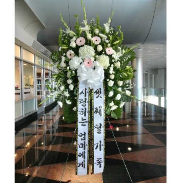 Large standing sympathy spray with white and pale pink flowers and long message ribbons on an easel.