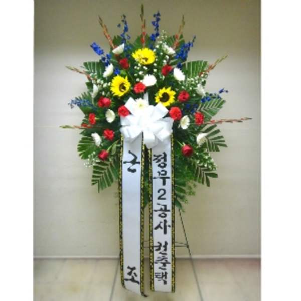 Tall standing spray with yellow sunflowers, red carnations, and white flowers on an easel