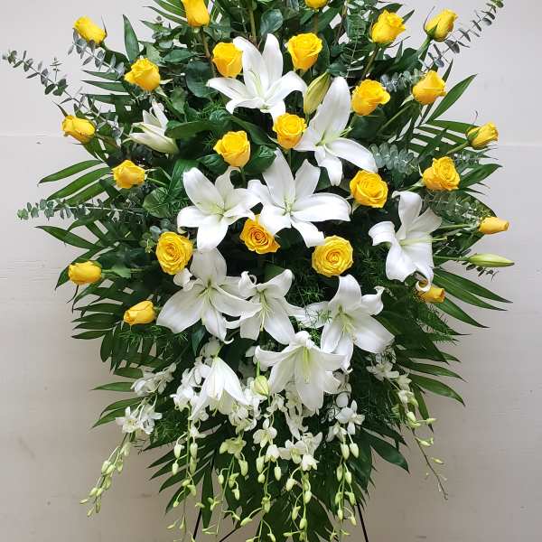 Standing spray of yellow roses and white lilies with cascading orchids on an easel