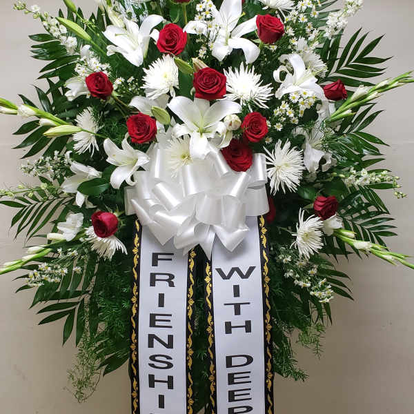 Standing sympathy spray with red roses, white lilies, and ribbon banners