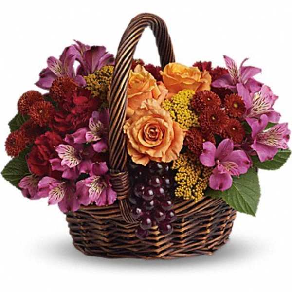 Low basket of orange roses and purple alstroemeria with fall-toned blooms and decorative grapes