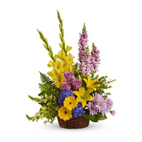 Tall mixed arrangement of yellow lilies and gerberas, purple roses, snapdragons, and blue hydrangea in a wicker basket