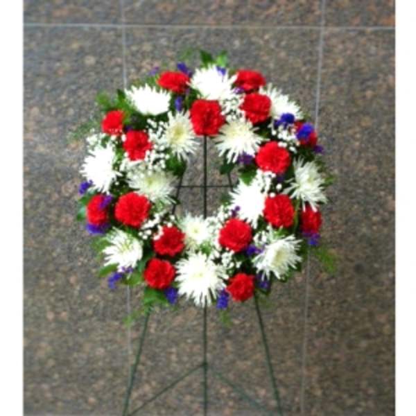 Standing wreath of red carnations and white mums with blue accents on a metal easel