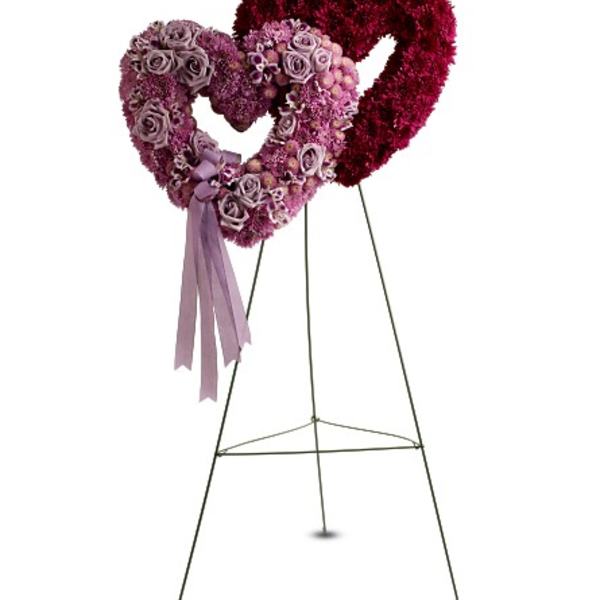 Two intertwined pink and purple heart-shaped floral wreaths on a tall easel stand.