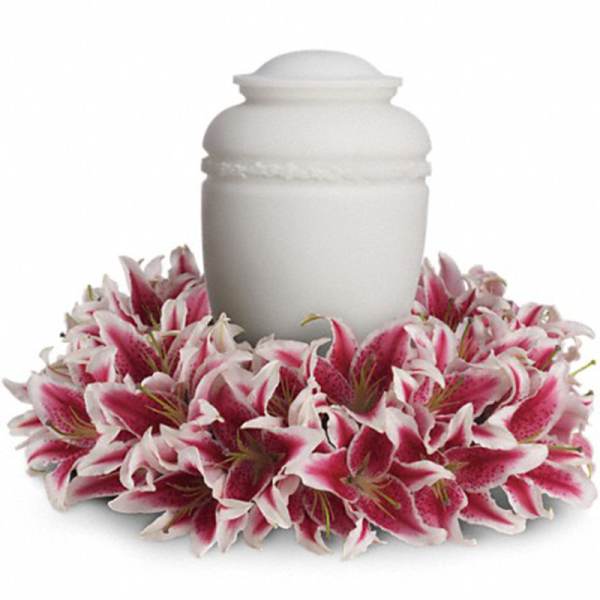 Pink lilies arranged in a circular wreath around a white cremation urn