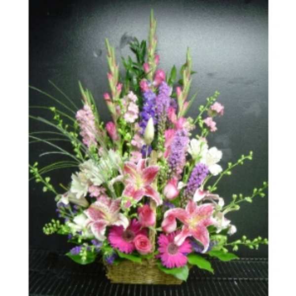 Tall pink and purple mixed flower arrangement in a wicker basket
