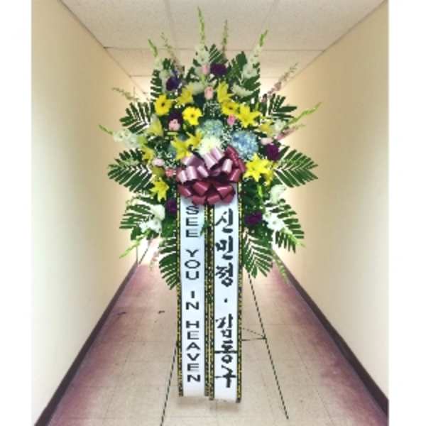 Tall standing funeral spray with yellow lilies, mixed blooms, and message ribbons on an easel