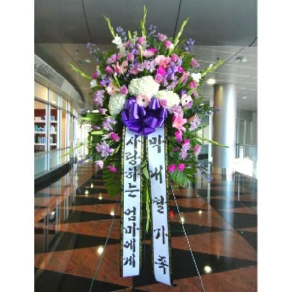 Tall standing spray of pink, purple, and white flowers with ribbons and a purple bow on an easel