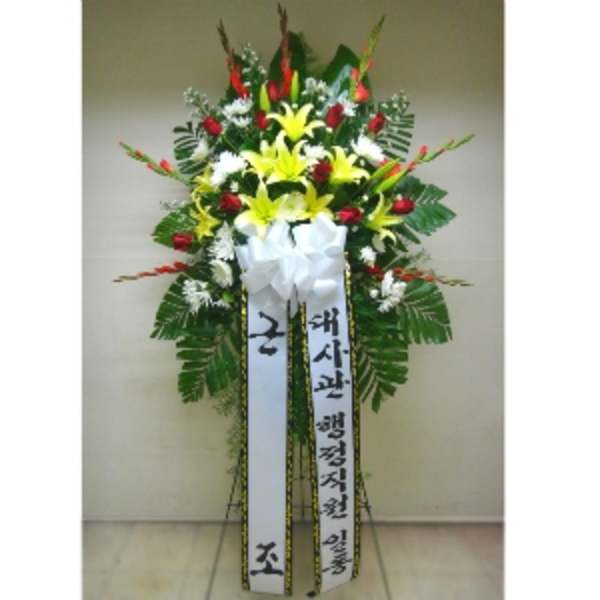 Tall standing spray with yellow lilies, red roses, white flowers, and long message ribbons in Korean.
