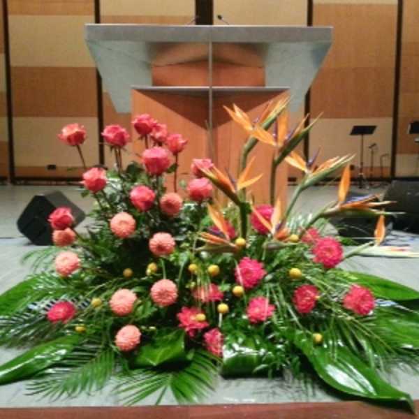 Large stage arrangement with pink roses, round pink blooms and orange tropical flowers in front of a podium