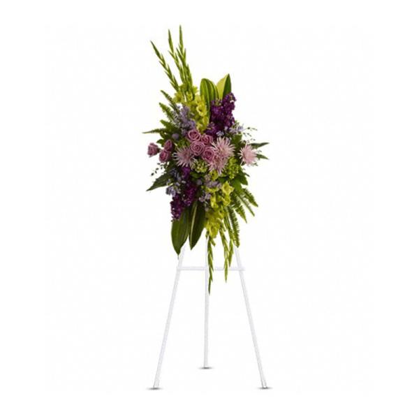 Tall standing spray of purple, lavender, and green flowers displayed on a white easel