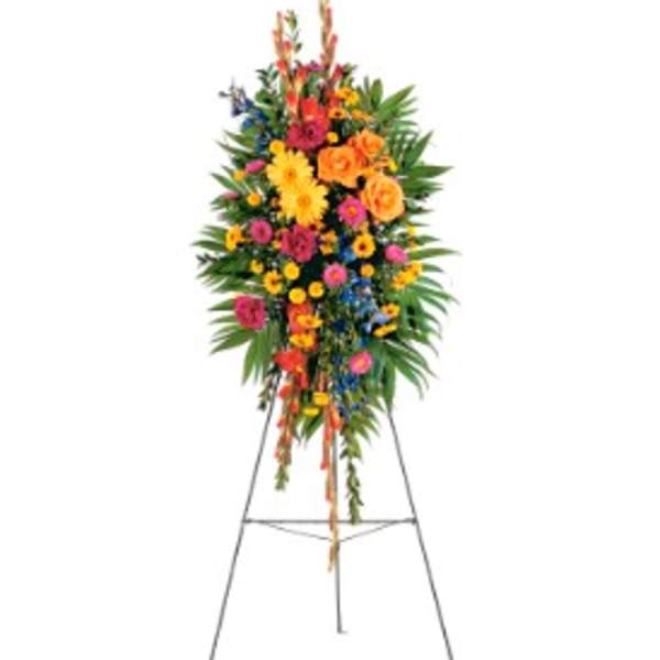 Tall multicolor standing spray with yellow gerbera daisies, orange roses, and mixed flowers on an easel