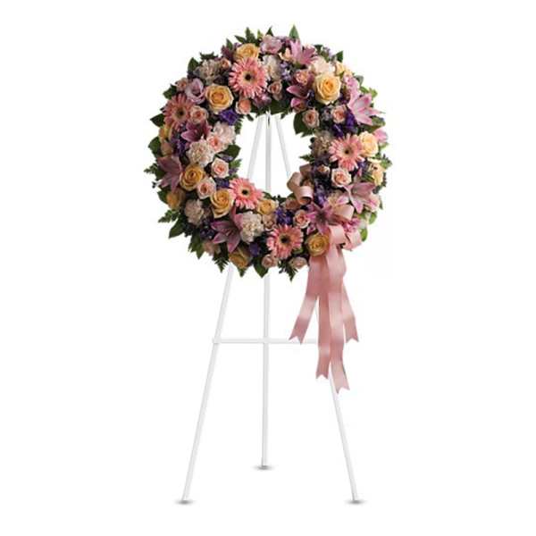 Pastel pink and peach standing funeral wreath with roses and gerbera daisies on a white easel with a pink bow
