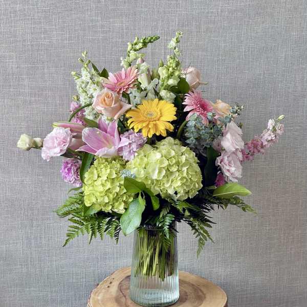Mixed bouquet with pink, yellow, and green flowers in a glass vase