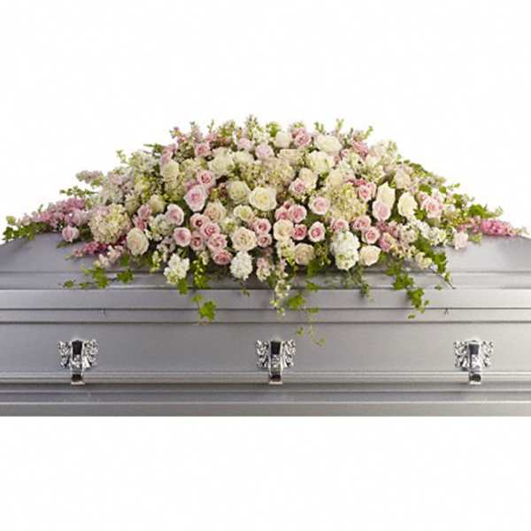 Full casket spray of soft pink and white flowers arranged across a silver casket