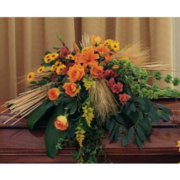 Autumn casket spray with orange roses, lilies, yellow daisies, and wheat on a wooden casket