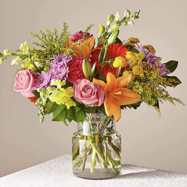 Mixed bouquet of pink roses, lilies, and colorful daisies in a glass vase