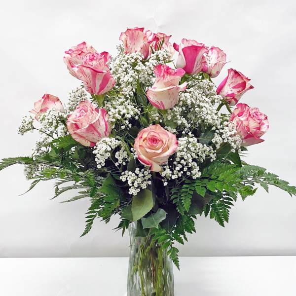 Tall clear vase of pink-tipped white roses with small white filler flowers.