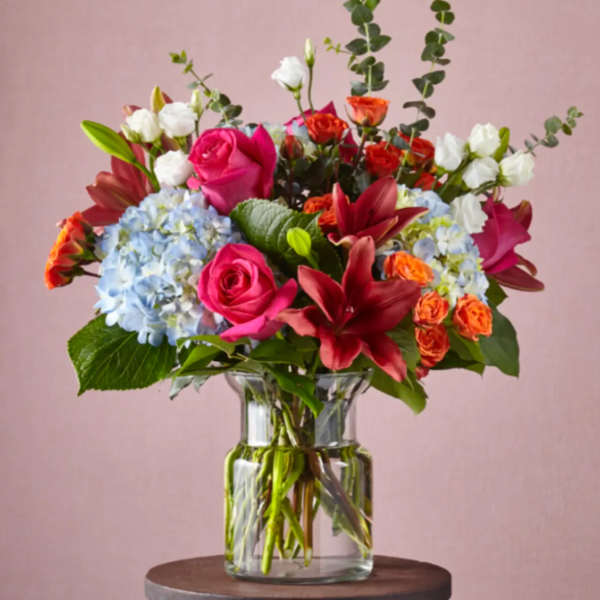 Mixed bouquet with pink roses, red lilies, blue hydrangeas and orange spray roses in a clear glass vase