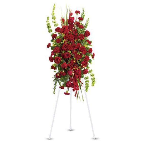 Tall red and green standing spray of roses and carnations displayed on a white easel.
