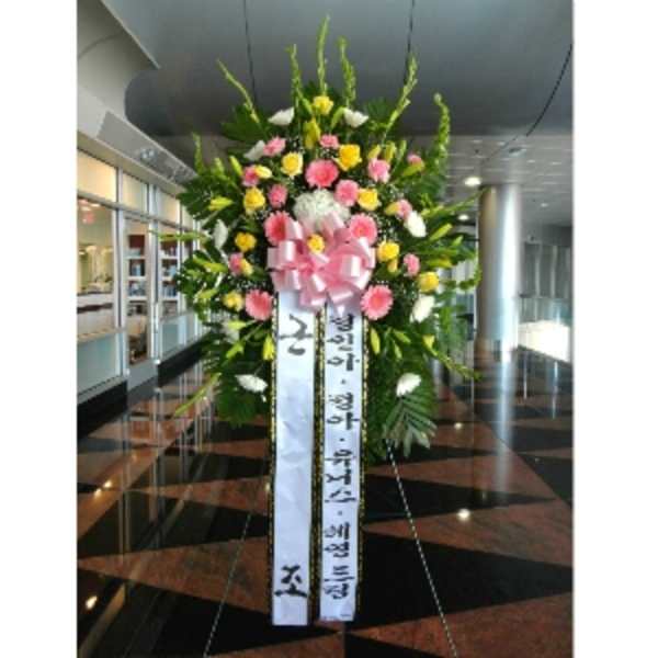 Tall standing spray of pink, yellow, and white flowers with a large pink bow and Korean message ribbons