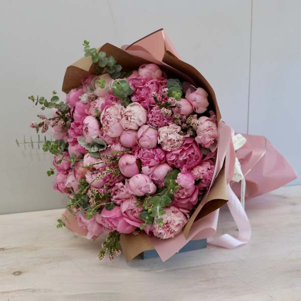 Large bouquet of pink peonies wrapped in pink and kraft paper with ribbon accents