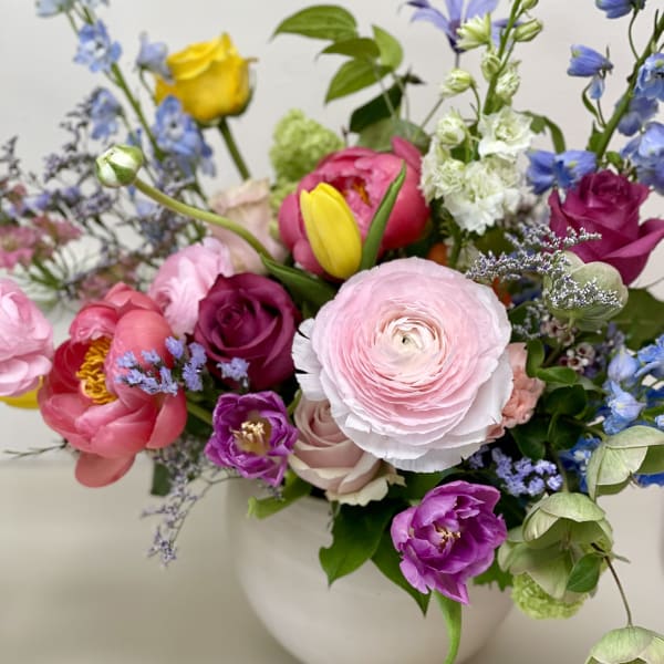 Mixed bouquet of pink, purple, yellow, and blue flowers in a white vase