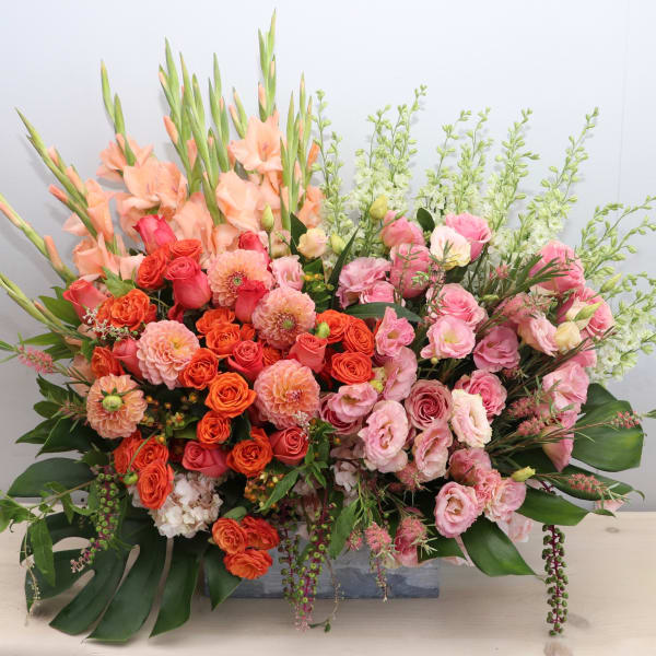 Large rectangular arrangement of peach gladiolus, orange dahlias, and pink roses in a low wooden container