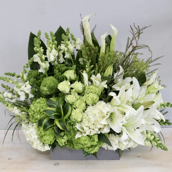 Large white and green arrangement with lilies and hydrangeas in a low gray rectangular container