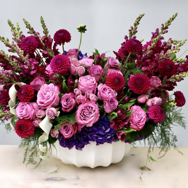 Low pink and magenta arrangement of roses, dahlias, and snapdragons in a white ceramic bowl