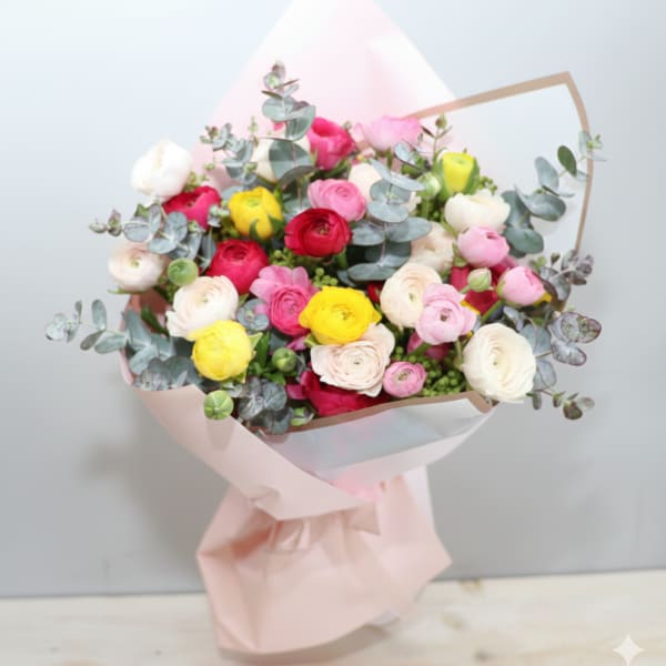 Hand-tied bouquet of pink, red, yellow and cream ranunculus wrapped in pale pink paper