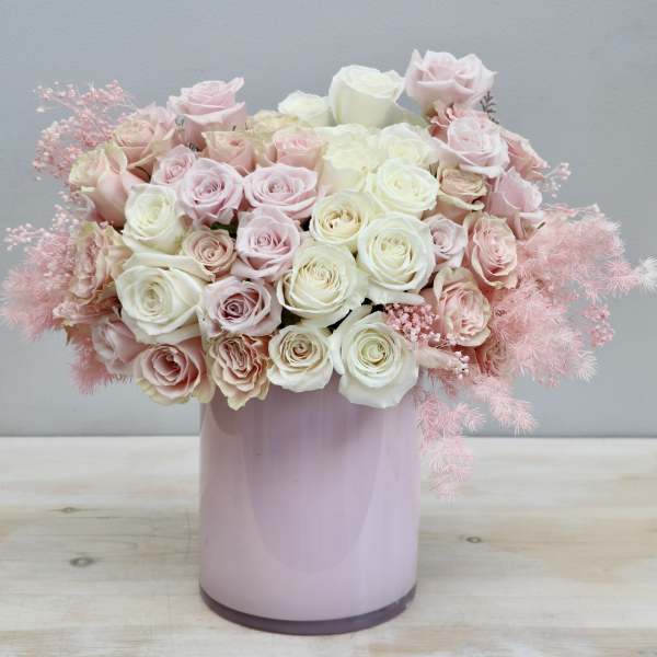 Tight arrangement of cream and blush roses in a pastel pink cylinder vase
