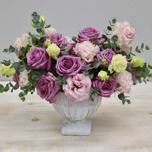 Low centerpiece of purple roses and pastel carnations in a white pedestal bowl