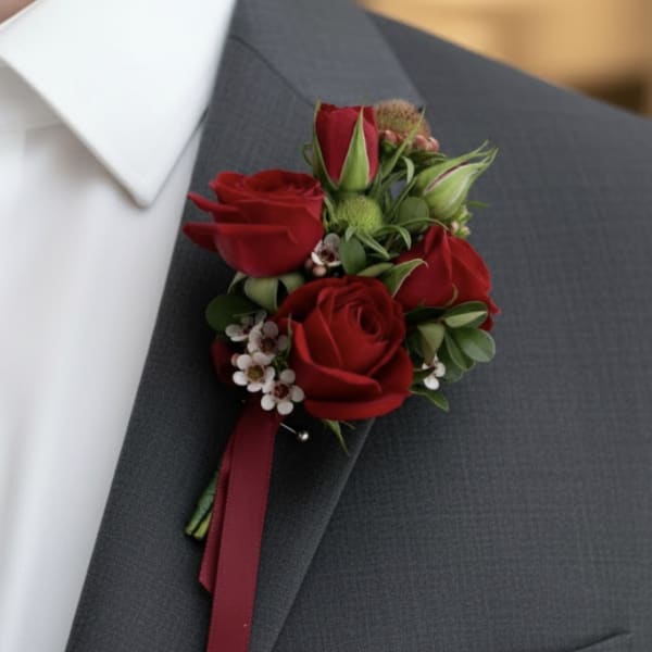 Red rose boutonniere with small white flowers pinned to a gray suit jacket lapel.