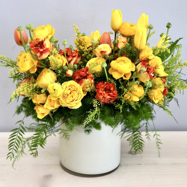 Bright yellow and orange mixed flower arrangement in a white cylinder vase