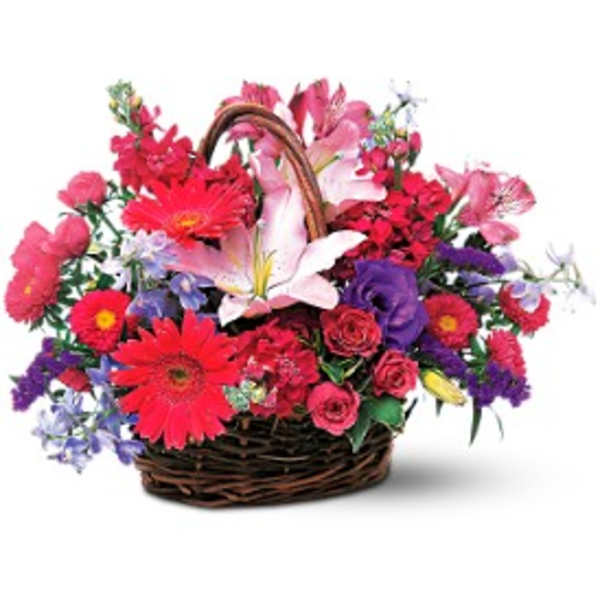 Bright mixed basket of pink lilies, red gerbera daisies, roses, and purple blooms in a brown wicker basket