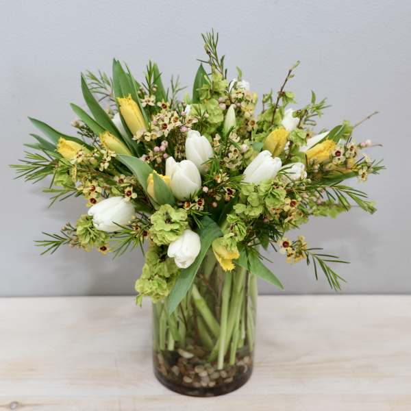 Springy arrangement of white tulips and yellow flowers in a glass cylinder vase with pebbles