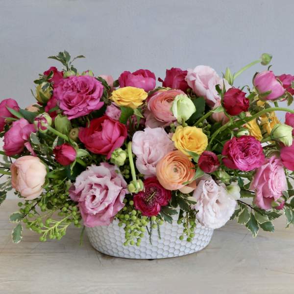 Low centerpiece of bright pink, yellow, and peach blooms in a white ceramic bowl.