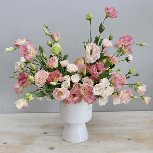 Low wide arrangement of pink lisianthus and blush spray roses in a modern white ceramic vase