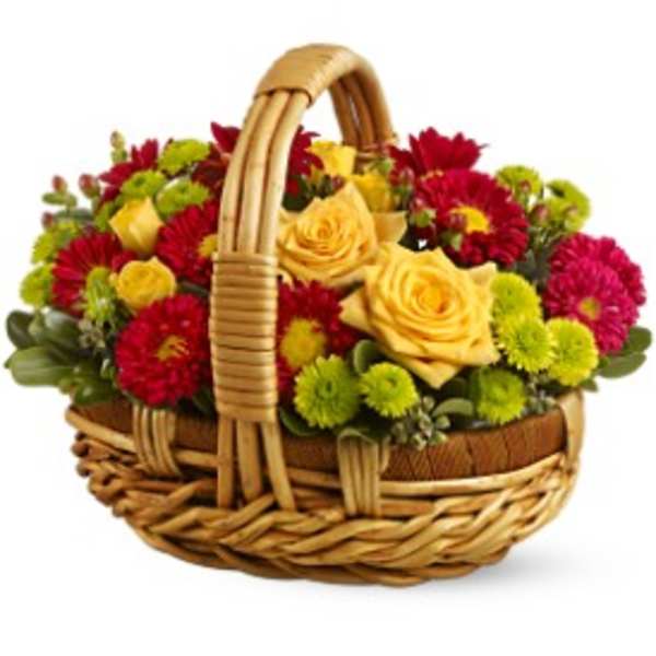 Low basket arrangement of yellow roses with red, pink, and green mums.