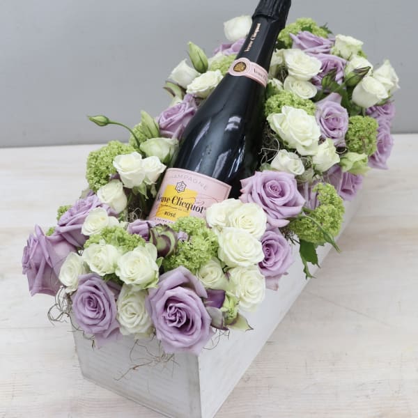 Rectangular box of lavender and white roses surrounding a rosé champagne bottle