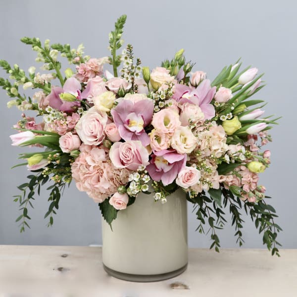 Large pastel pink and white flower arrangement with roses, orchids, and tulips in a white cylinder vase