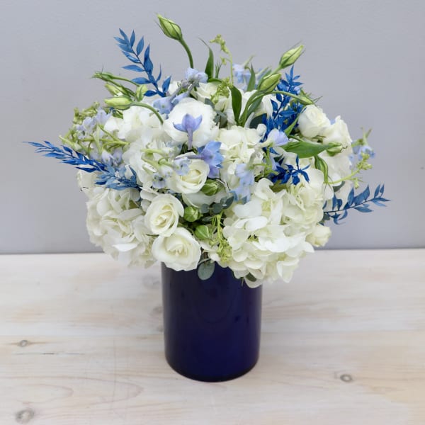 White and light blue flower arrangement in a dark blue cylinder vase
