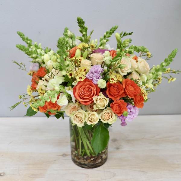 Vase arrangement of orange and cream roses with snapdragons and touches of yellow and lavender flowers