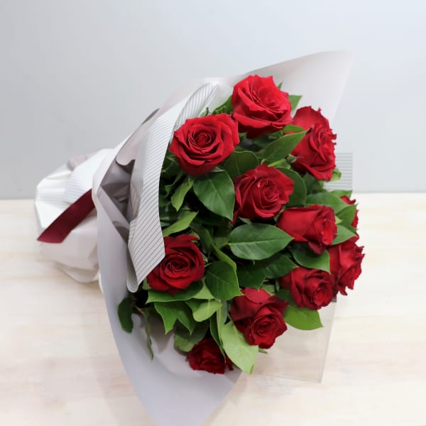 Hand-tied bouquet of red roses wrapped in white paper with a red ribbon