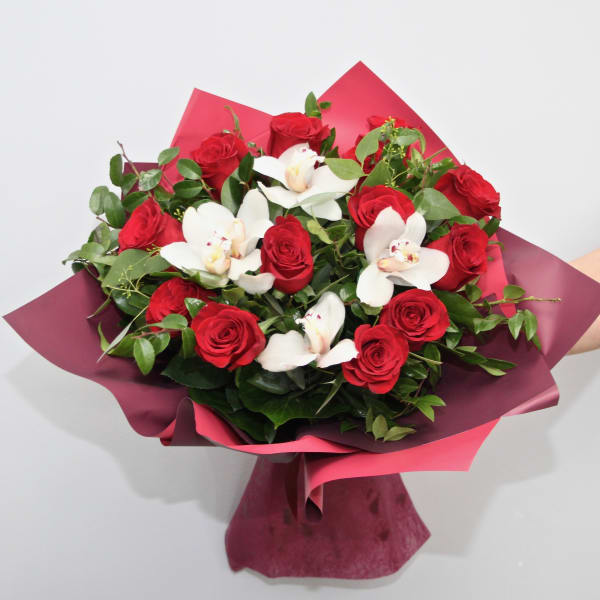 Hand-tied bouquet of red roses and white orchids wrapped in burgundy and pink paper