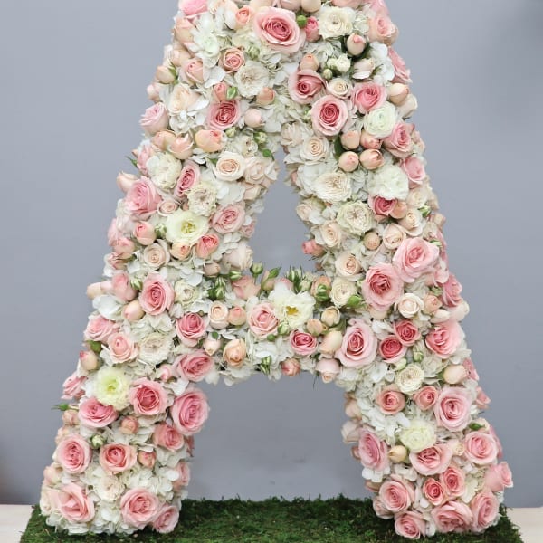 Tall floral letter A made of soft pink and white roses and hydrangeas on a moss-covered base